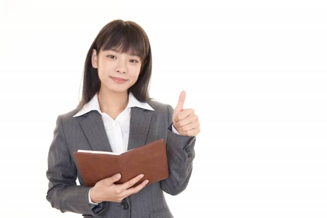 本を持ちサムズアップするビジネスパーソン